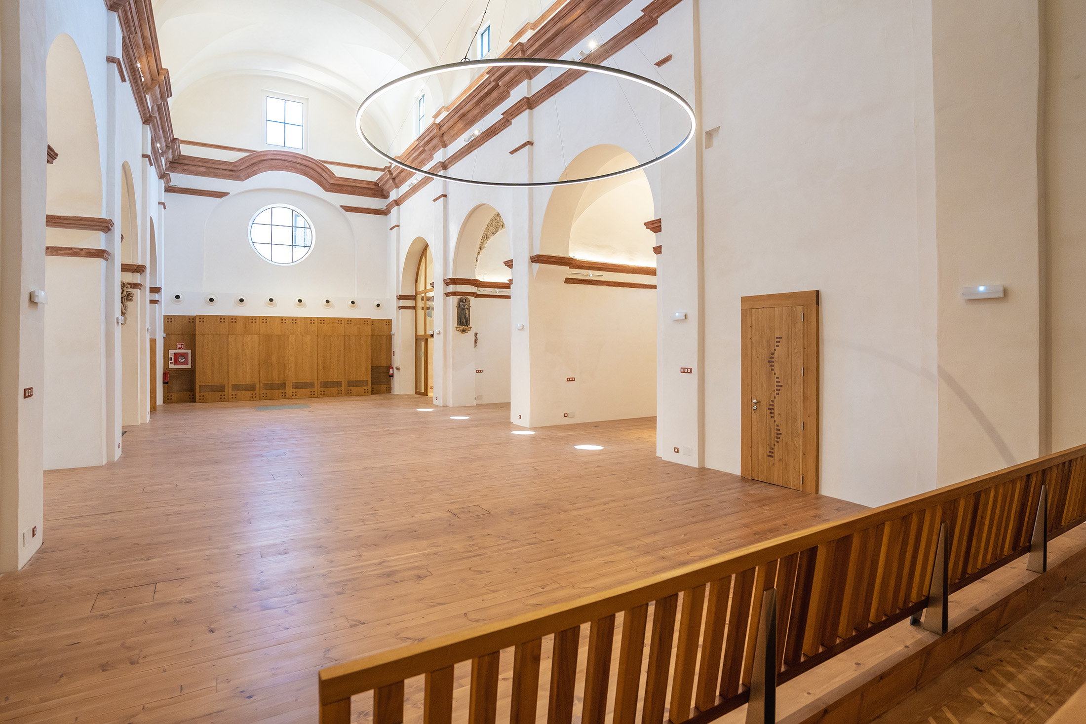 Vista general de la nave central diáfana con suelo de madera y lámpara circular moderna